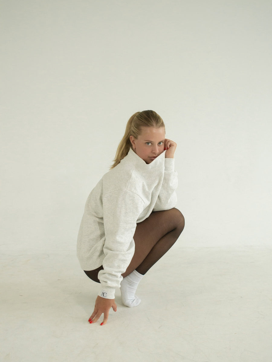 Ballet Rodeo heather-grey mockneck sweatshirt worn crouching, with black tights and white socks